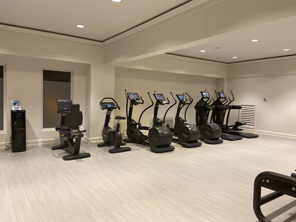 Una palestra con diverse tapis roulant affiancati, un distributore d'acqua e una piccola scrivania con un portatile.
