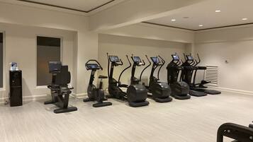 Una palestra con diverse tapis roulant affiancati, un distributore d'acqua e una piccola scrivania con un portatile.