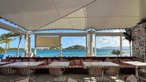 An outdoor seating area with tables and chairs, overlooking a body of water and a distant island. - BEACHFRONT LUXURY at the Ritz! NEWLY RENOVATED - MOST DATES Available! (Nazareth)