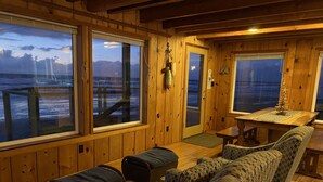 A wooden cabin interior with large windows overlooking a dock and water. There is a sofa, a small table, and a bench. - Oceanfront, Private Beach Access, Newly Updated, Perfect for Family Gatherings! (Lincoln City)