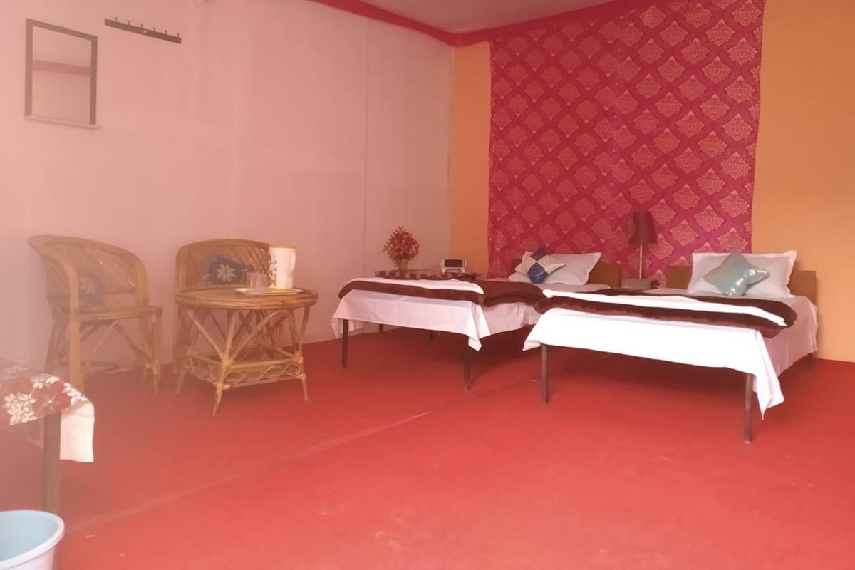 Ein Zimmer mit zwei Betten, einem kleinen Tisch, zwei Stühlen und einem roten Teppich.