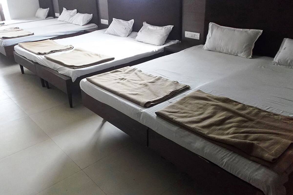 Ein Hotelzimmer mit drei Einzelbetten, jedes mit weißen Leintüchern und einer beigen Decke.