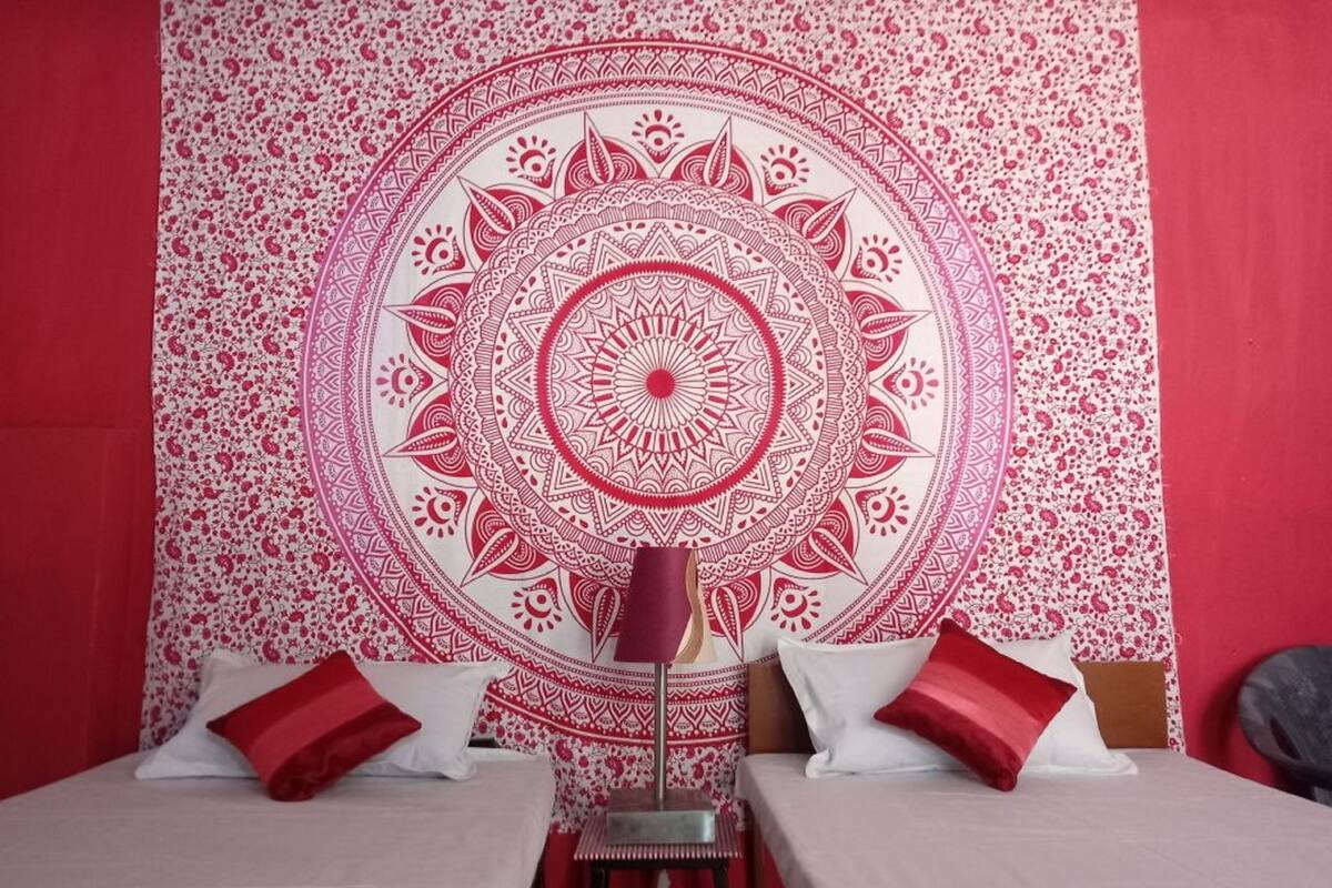 Ein Zimmer mit einer großen roten und weißen Wandteppich, zwei Betten mit roten und weißen Kissen und einem kleinen Tisch mit einer Lampe.