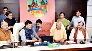 A group of people seated at a conference table with laptops and documents, in a room with a banner in the background. - Prayag Divine Kumbh Camp - Hostel (Karchana)