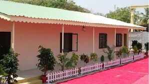 A building with a pink facade, a green roof, and a white picket fence. - Prayag Divine Kumbh Camp - Hostel (Karchana)