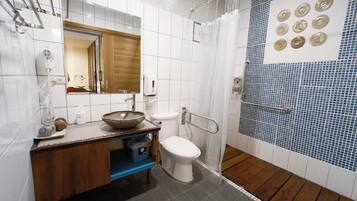 A bathroom with a white toilet, a wooden vanity, a sink with a bowl, a mirror, a hand dryer, and a shower with blue mosaic tiles.