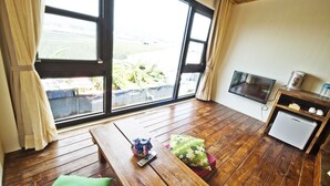 A room with a wooden floor, a small table with a remote control and a pillow, a television on the wall, and a mini fridge. - SHYE Lithuania Homestay (Taichung)