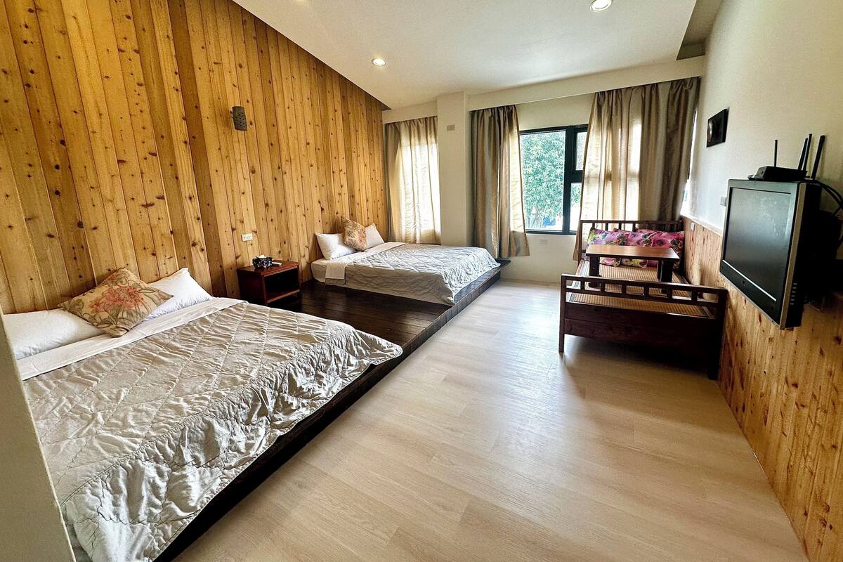 A hotel room with two beds, a wooden wall, a TV, and a window with curtains.
