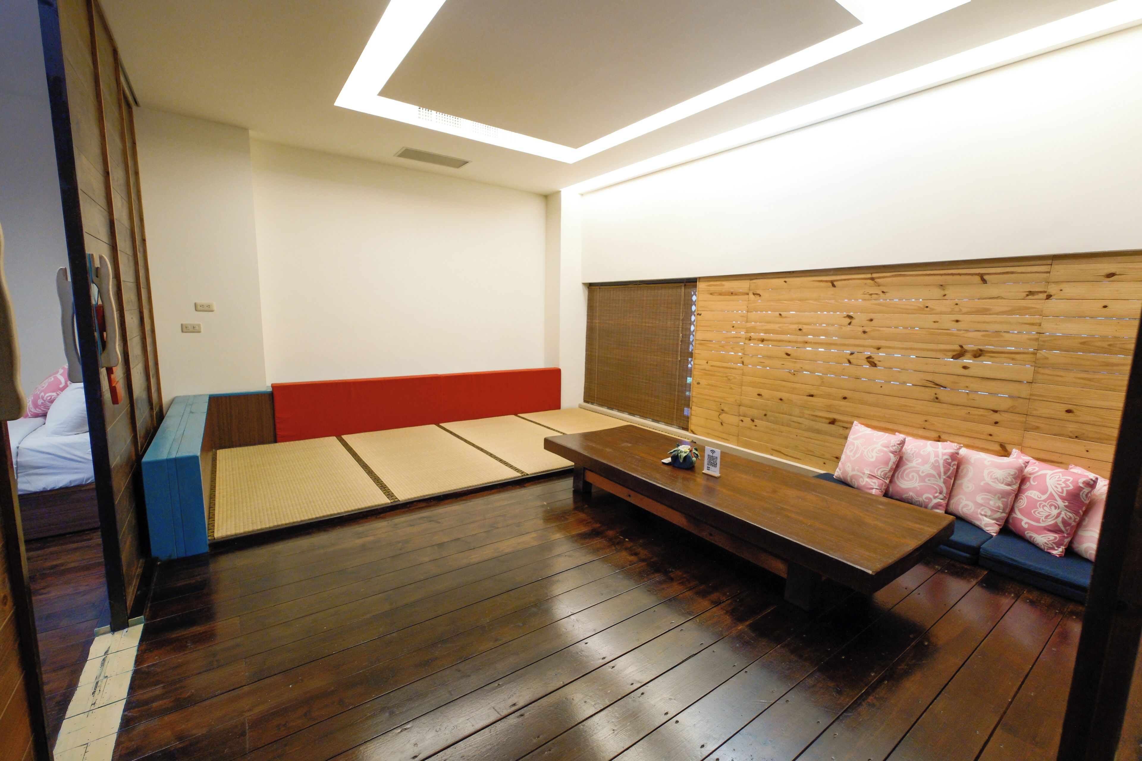 Een traditionele Japanse kamer met tatami vloerbedekking, een laag houten hoofdbord en een klein tafeltje met kussens.