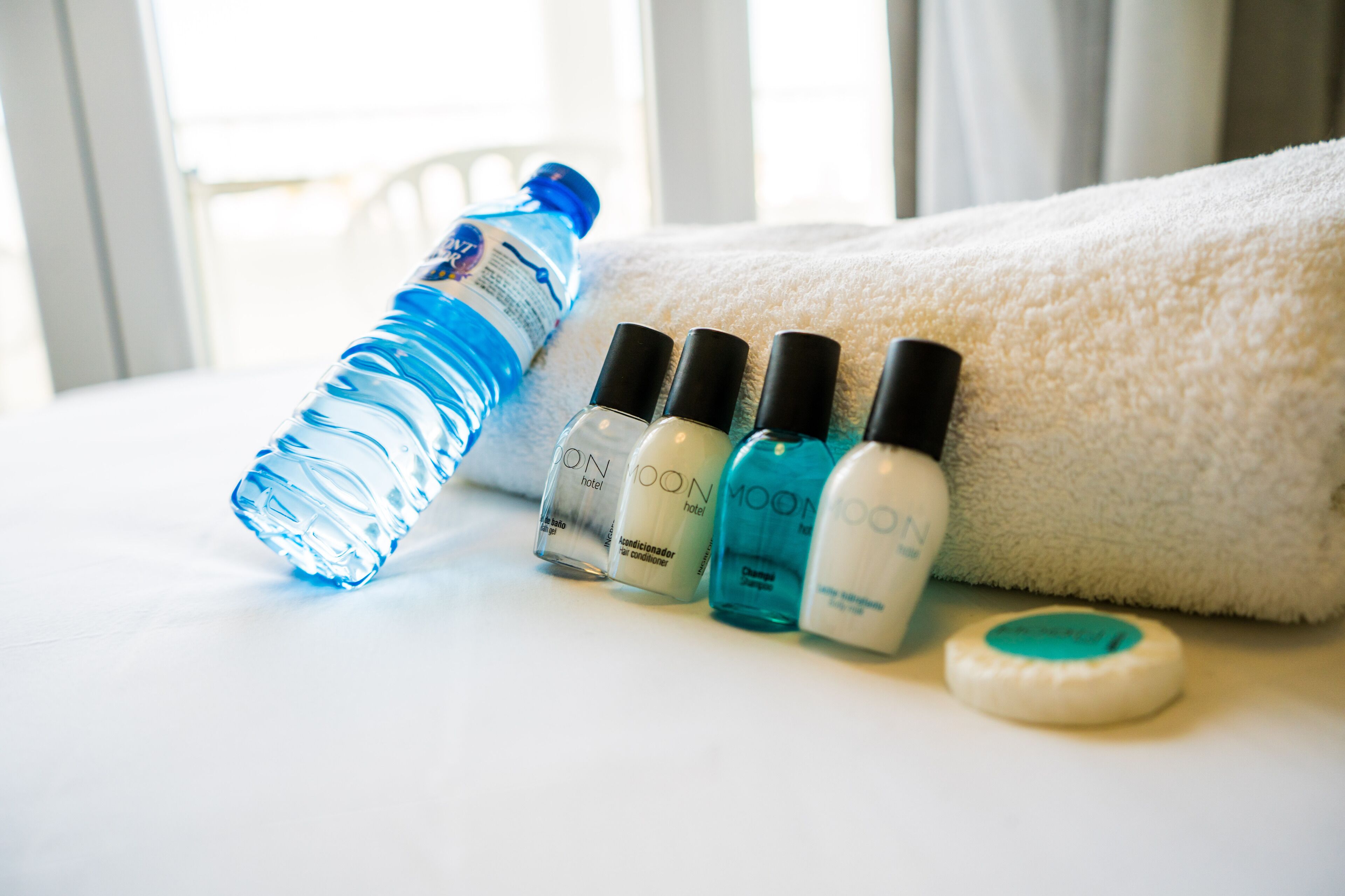 Una botella de agua, cuatro botellas de esmalte de uñas y una pastilla de jabón sobre una superficie blanca.