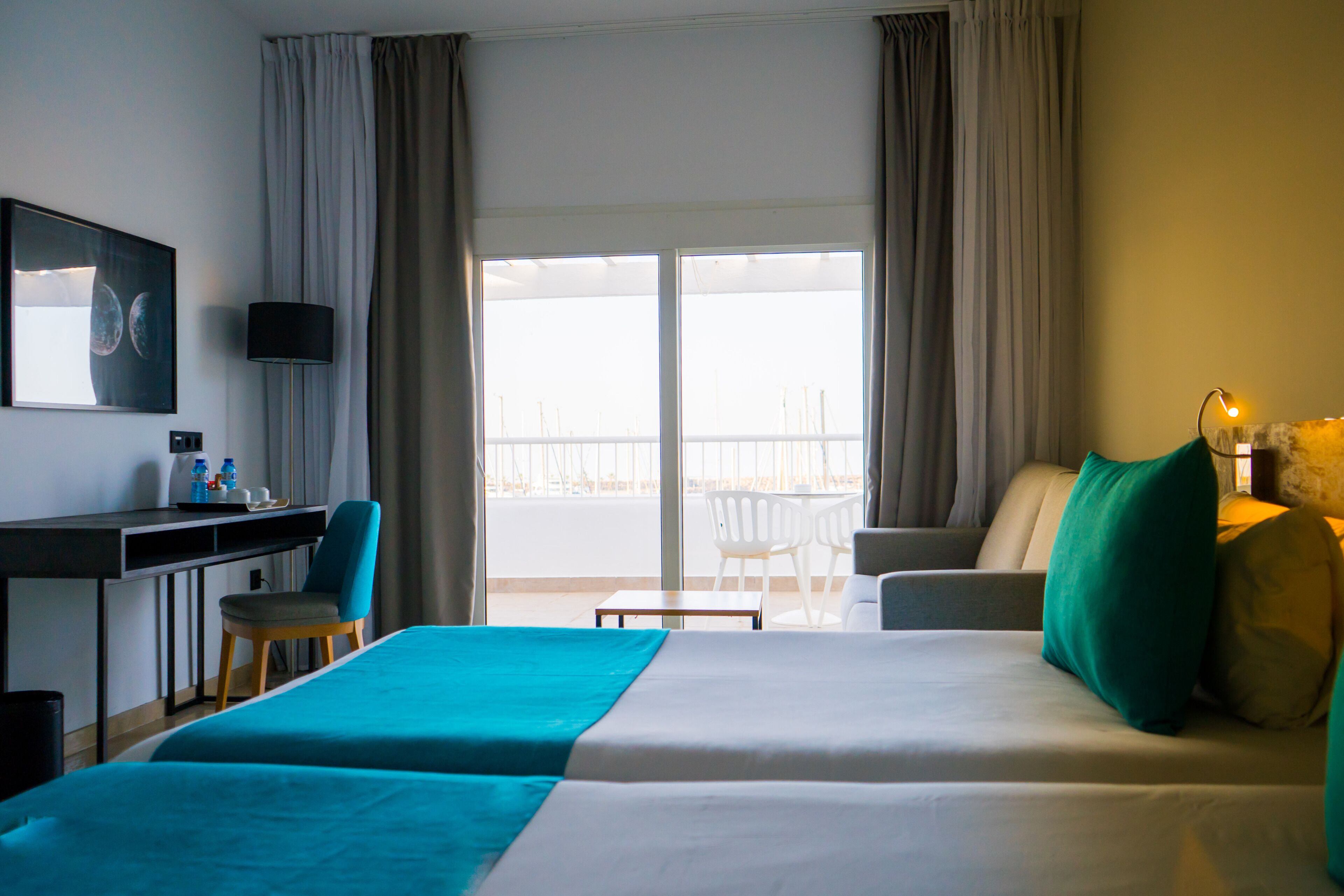 A hotel room with a bed, a desk, a chair, a table, and a balcony with a view.