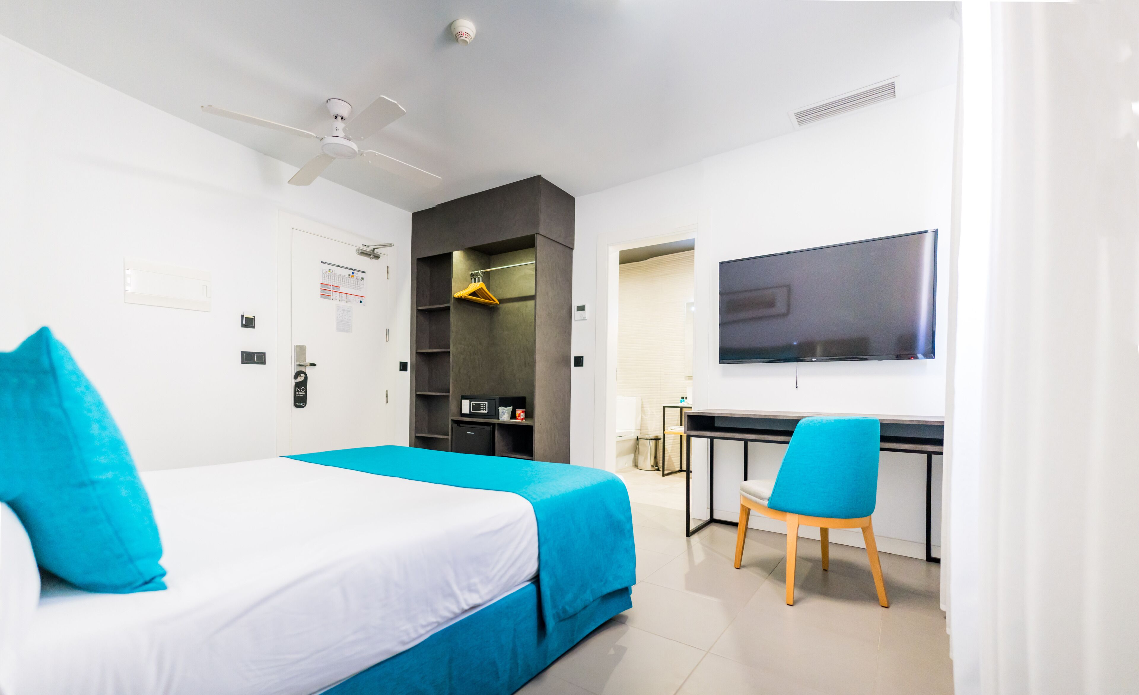 Una camera d'albergo con un letto, una scrivania, una sedia, una televisione e un armadio.