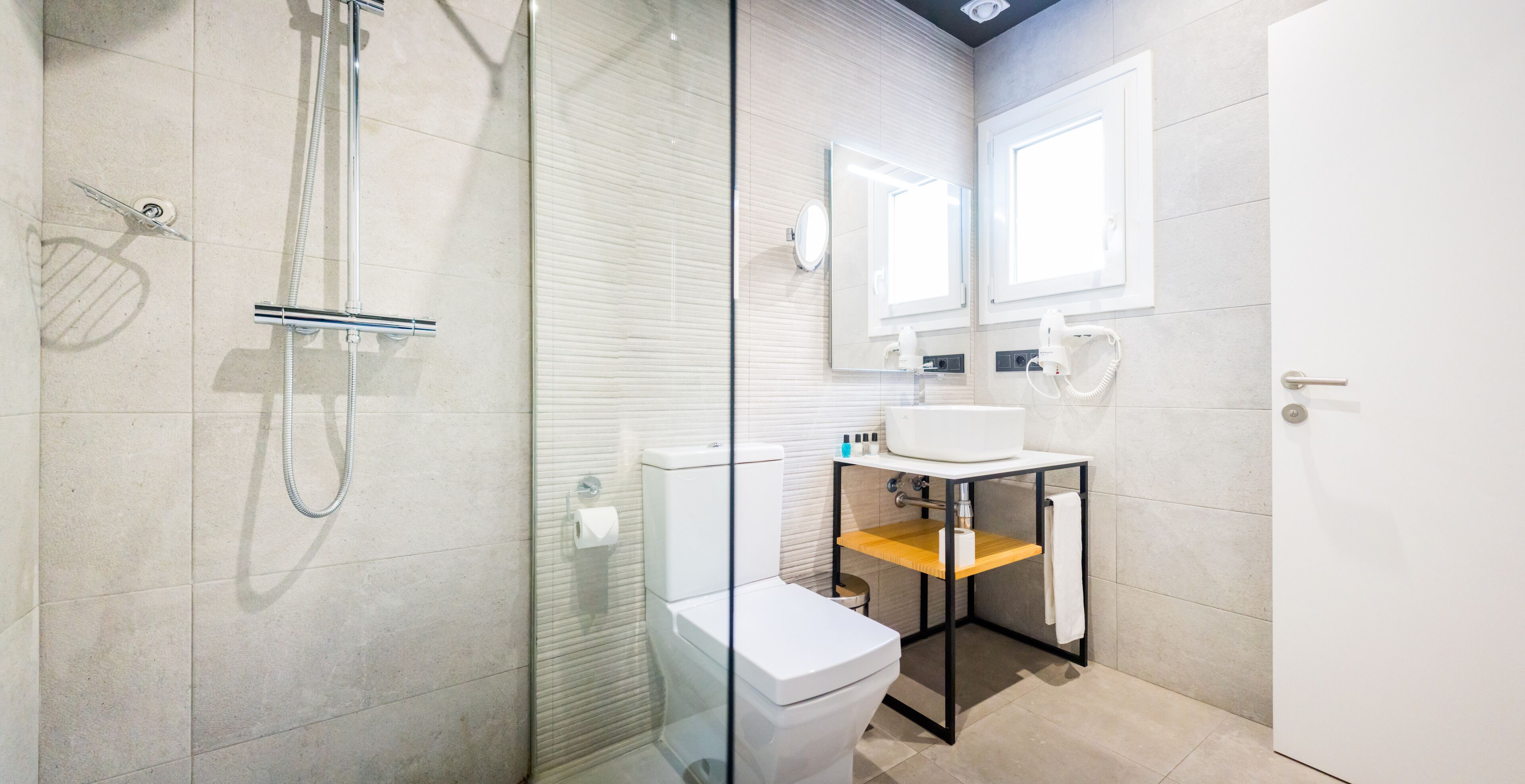 A modern bathroom with a glass shower enclosure, a white toilet, a wooden vanity with a sink, and a mirror above the mirror.