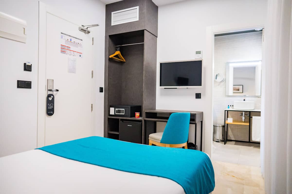 Une chambre d’hôtel équipée d’un lit, d’un bureau, d’une chaise, d’une télévision, d’un miroir et d’une petite kitchenette.