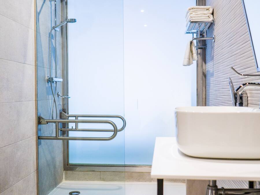 Un baño moderno con cabina de ducha de vidrio, un lavabo blanco y un perchero para toallas.