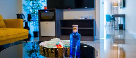 A modern living room with a round black table, a yellow sofa, a flat-screen TV, a plant, and a blue bottle.