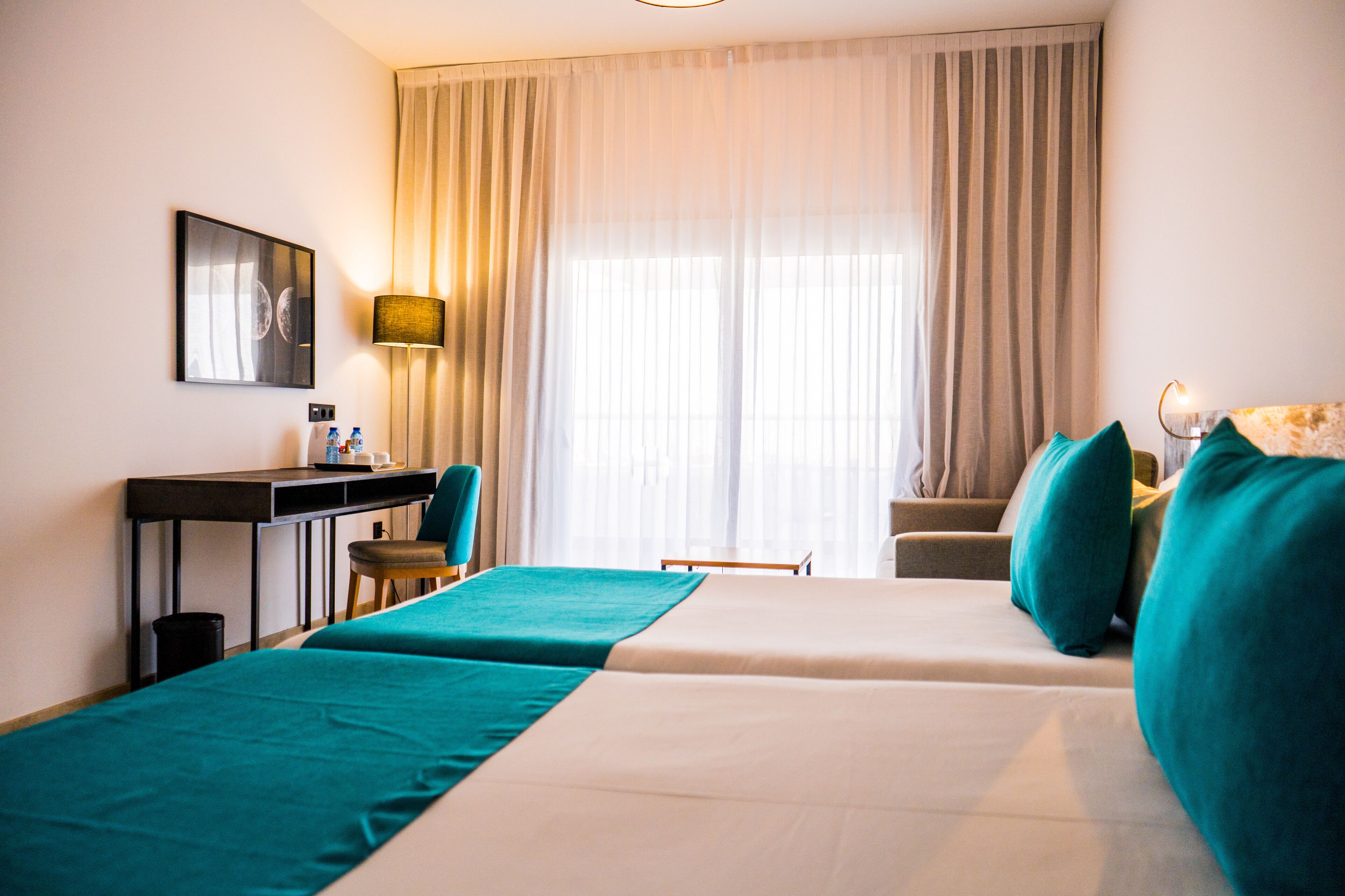 Une chambre d’hôtel avec deux lits, un bureau, une chaise et une grande fenêtre avec des rideaux.
