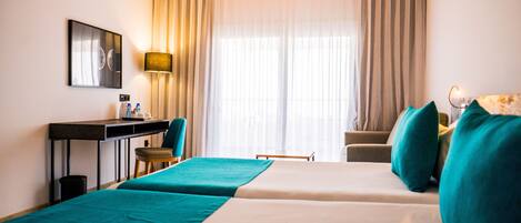 Habitación de hotel con dos camas, un escritorio, una silla y un ventanal con cortinas.