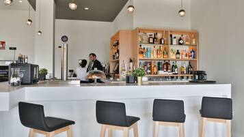 A modern bar area with a white counter, black bar stools, and a variety of liquor bottles.