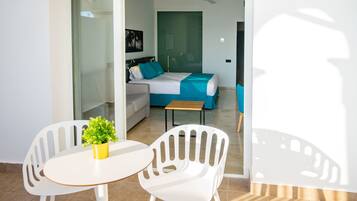 A modern hotel room with a balcony, a bed with blue bedding, a sofa, and a small table with a plant.