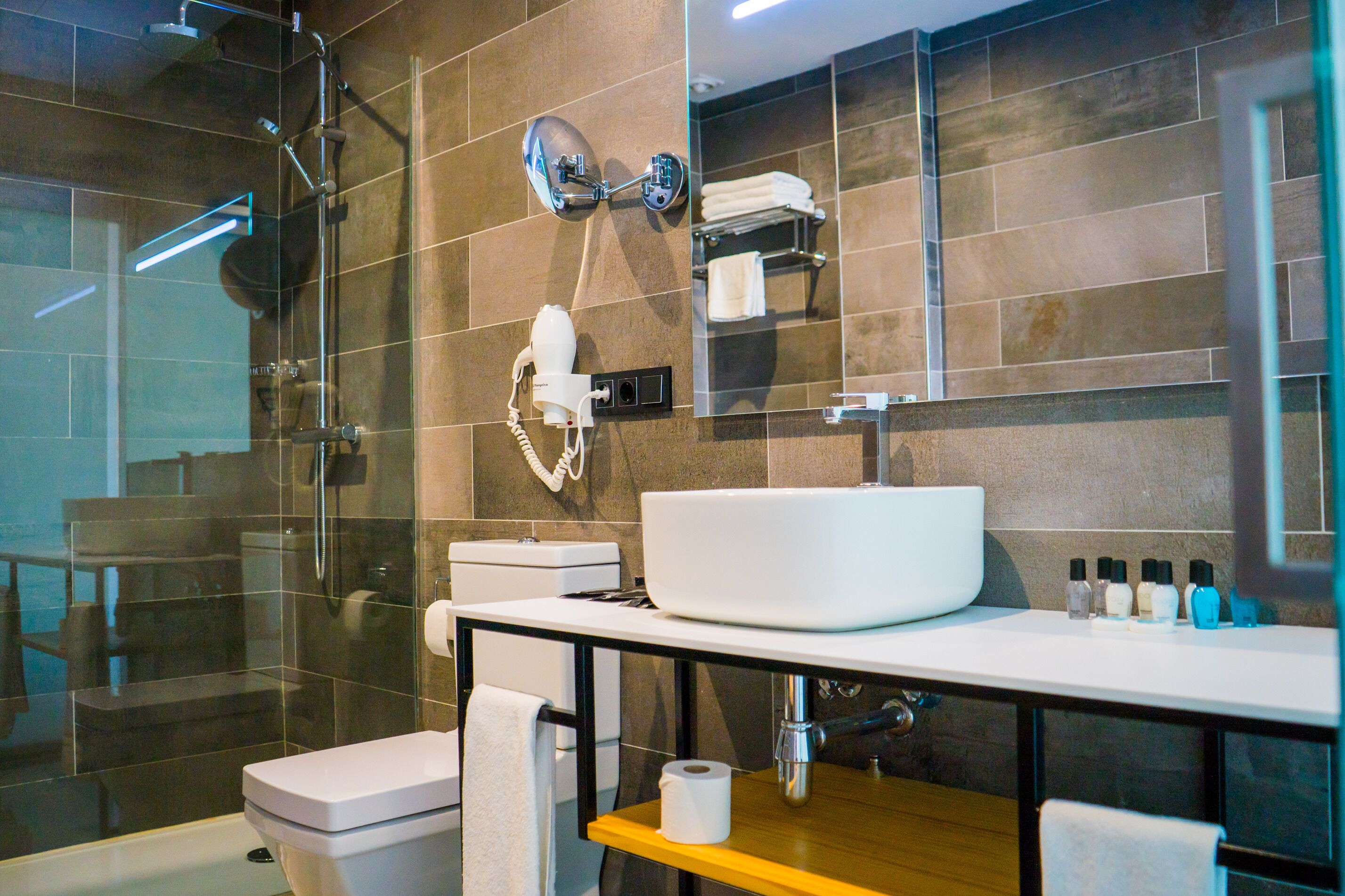 Un baño moderno con ducha de vidrio, un lavamanos blanco y un espejo sobre él.
