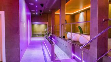 A modern hotel corridor with a purple-lit pathway, a glass railing, and a spa area with large tubs.