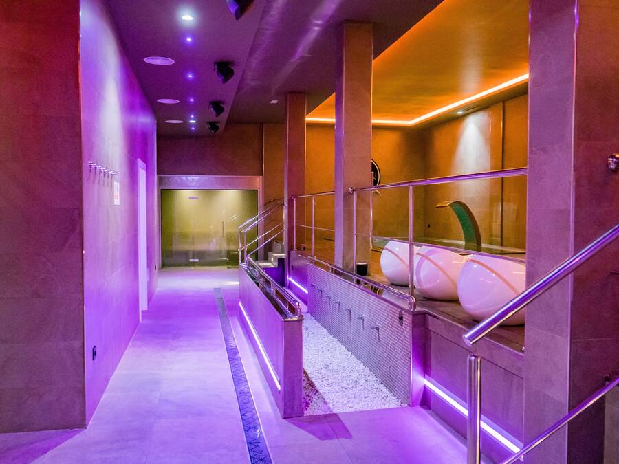 A modern hotel corridor with a purple-lit pathway, a glass railing, and a spa area with large tubs.