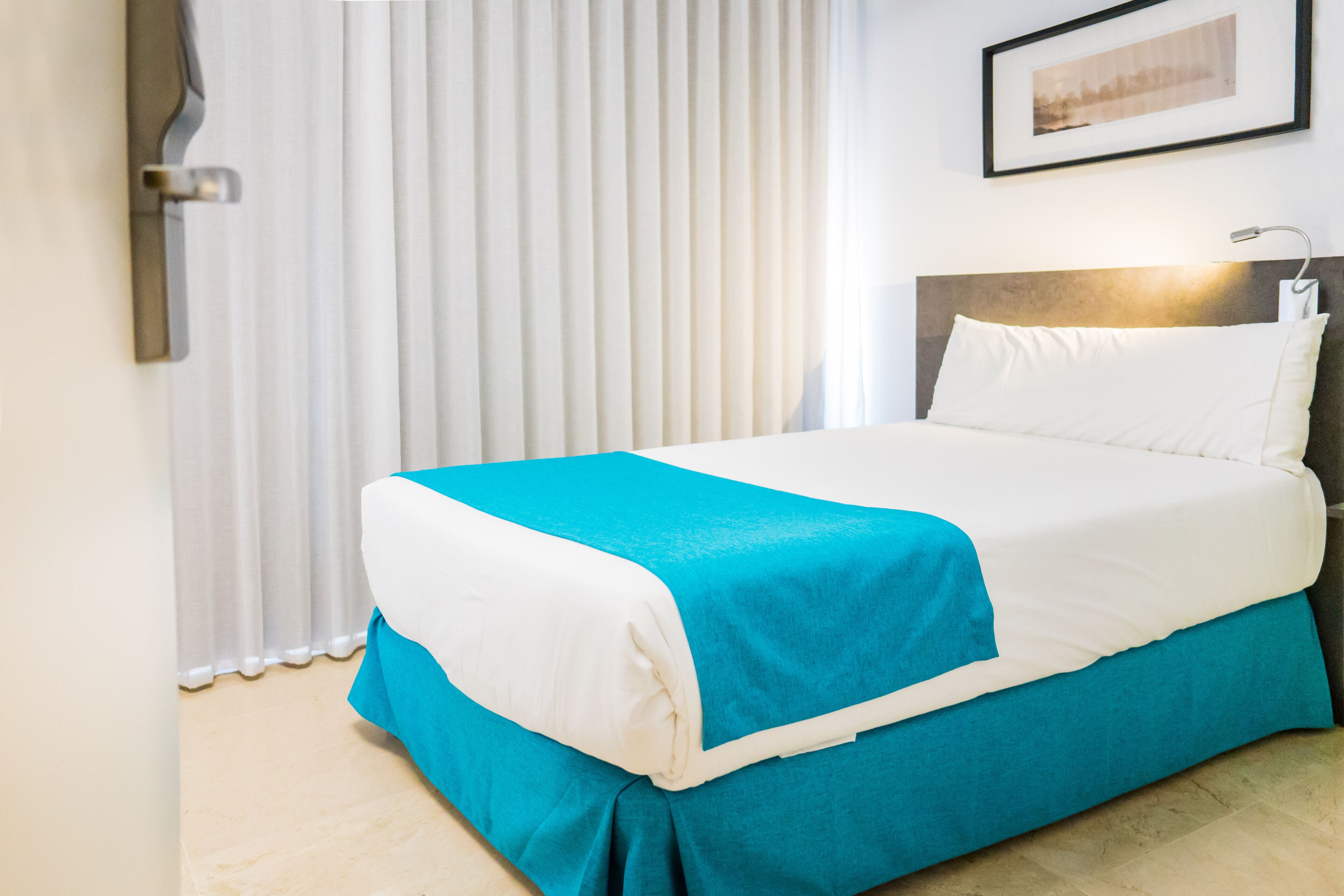 A neatly made bed with a white and blue bedspread, a headboard, and a wall-mounted light.