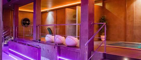 Un área de spa con un amplio jacuzzi, una recepción y una escalera que sube al piso superior.