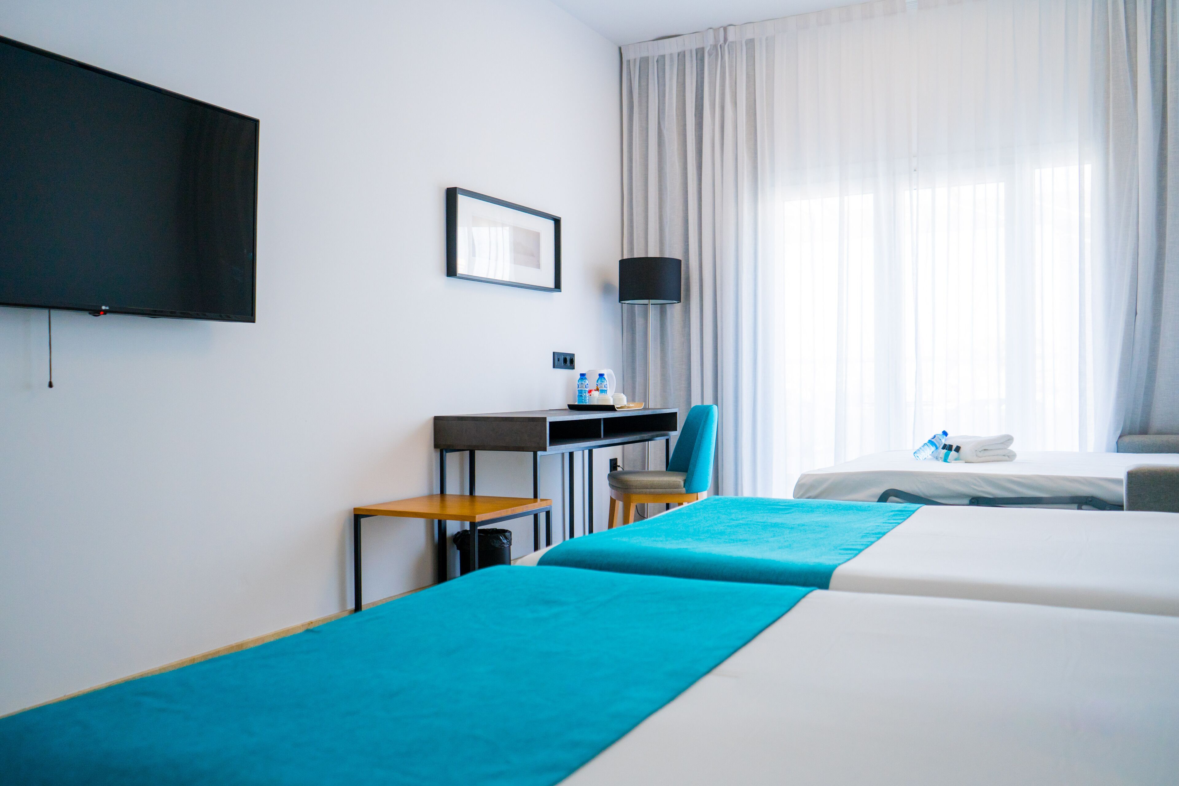 Habitación de hotel con dos camas, un escritorio, una silla, un televisor y una ventana con cortinas.