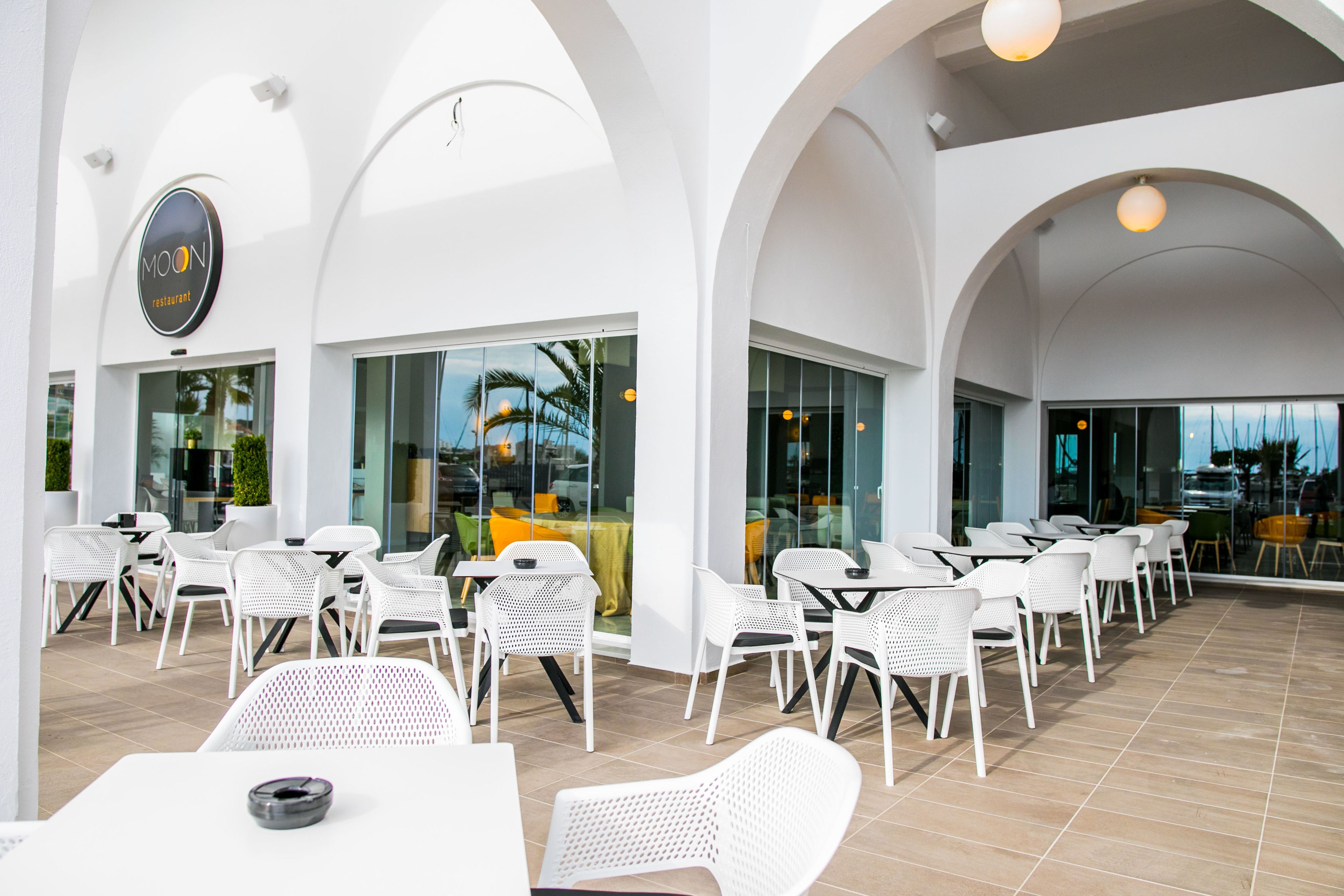 Un restaurant avec des meubles blancs et de grandes fenêtres.