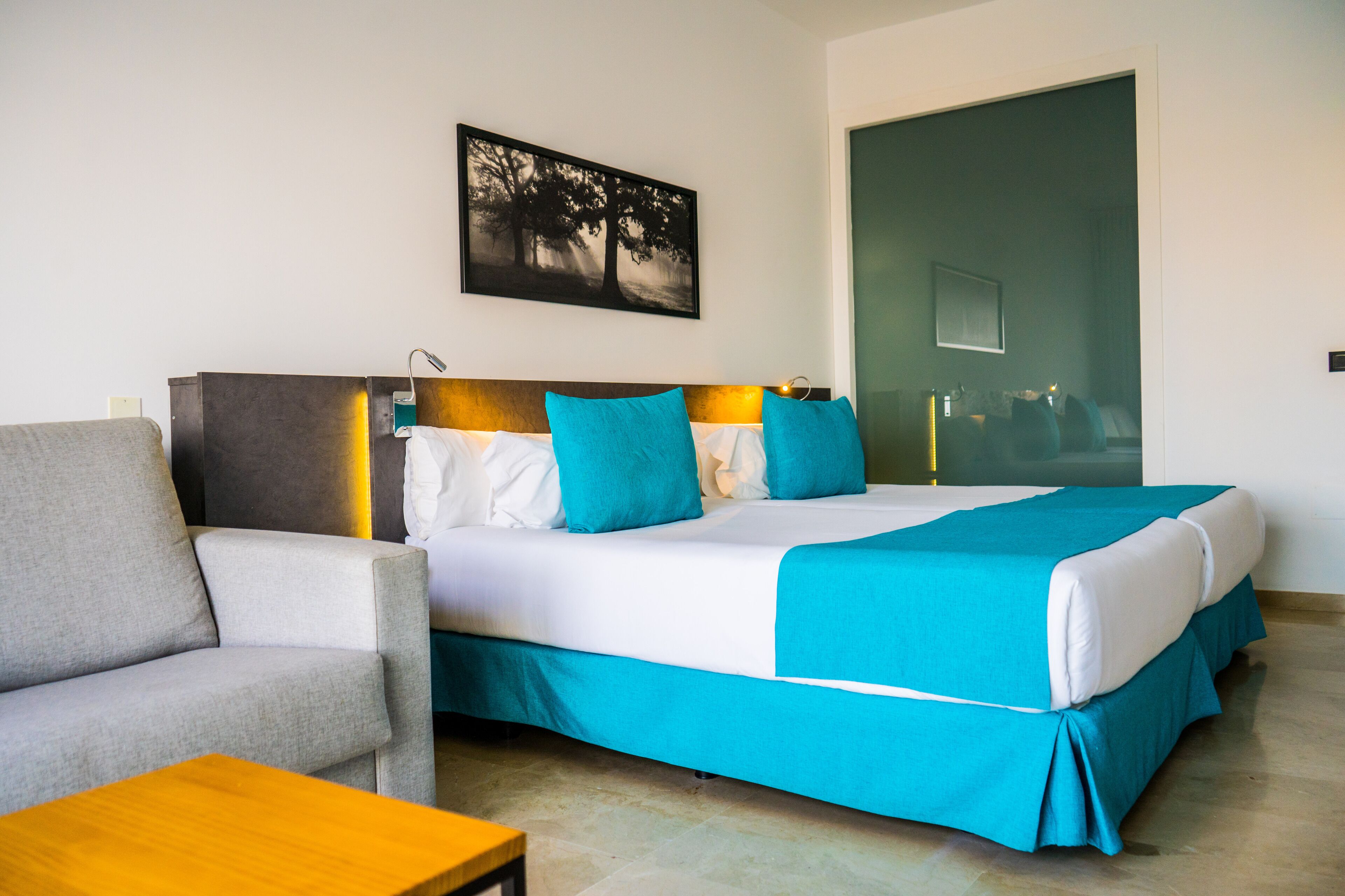 A hotel room with a bed, a sofa, a table, and a painting on the wall.