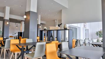 Un espace repas moderne avec des tables et des chaises, un bar et une vue sur l’extérieur.