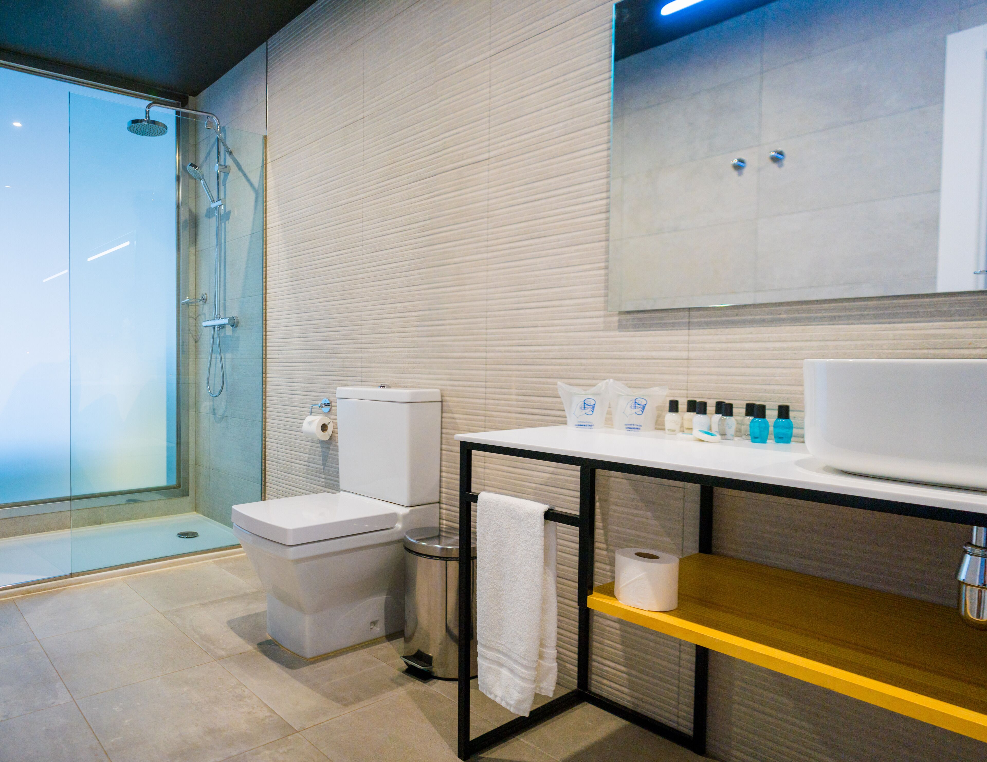Ein modernes Badezimmer mit einer Glasdusche, einer Toilette, einem Waschbecken mit Pflegeprodukten und einem Handtuchhalter.