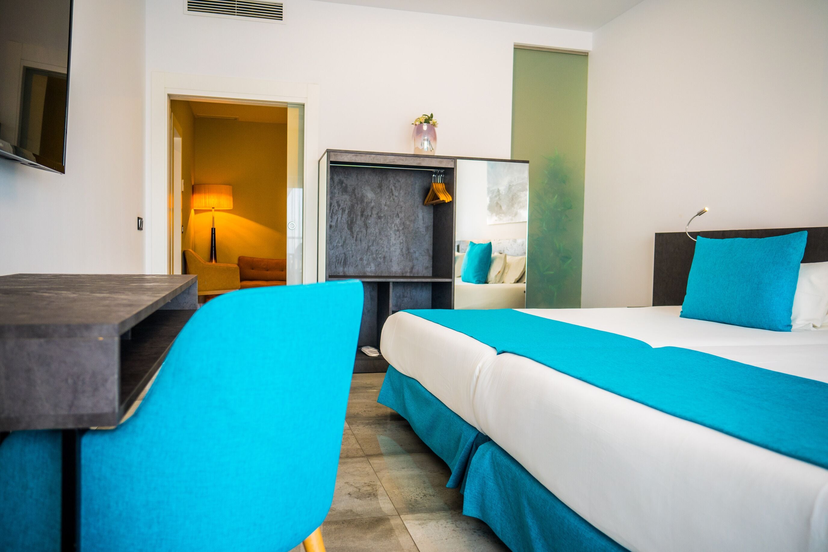 Una habitación de hotel con una cama, un escritorio, una silla, un televisor y una puerta que da a otra habitación.