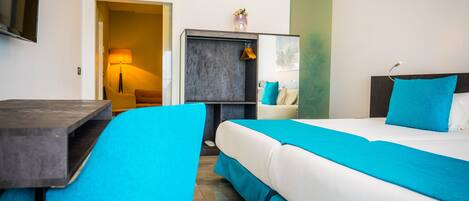 Una habitación de hotel con una cama, un escritorio, una silla, un televisor y una puerta que da a otra habitación.