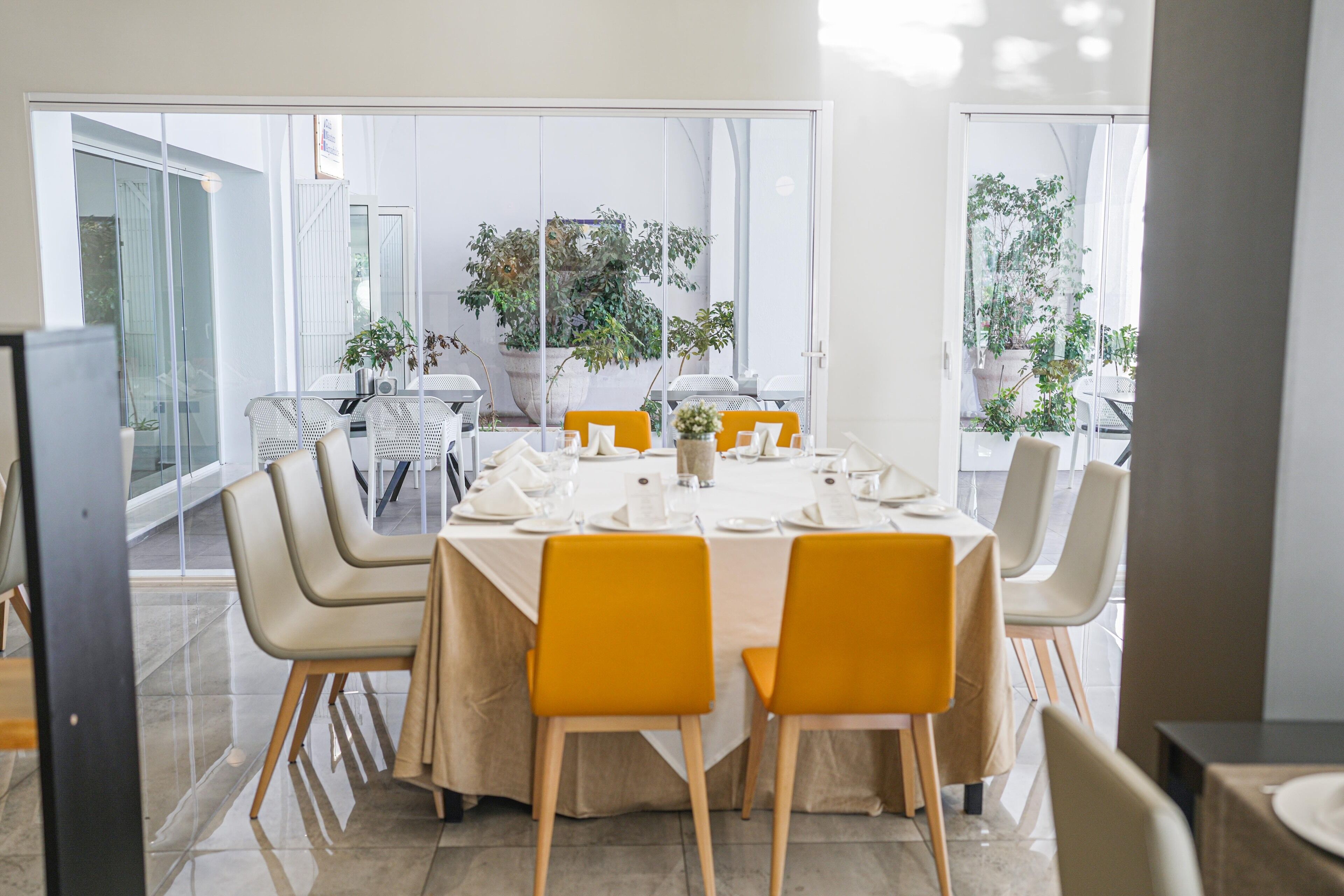 Un comedor con una mesa dispuesta para seis personas, rodeada de sillas y grandes ventanales con vistas al exterior.