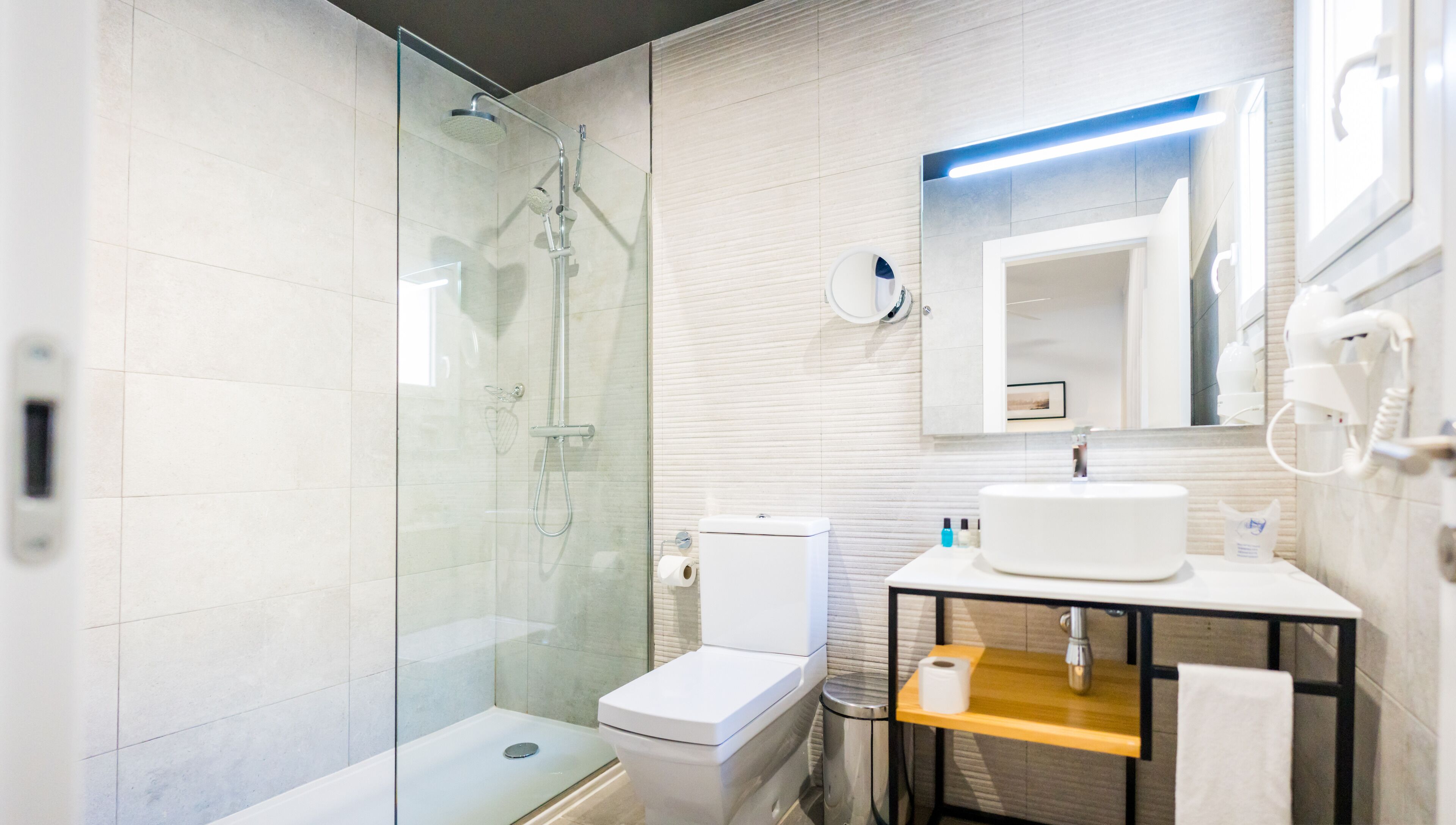 Un baño moderno con ducha envuelta en vidrio, inodoro, lavabo con espejo y un pequeño cubo de basura.