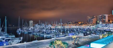 Un port de plaisance de nuit, avec des bateaux amarrés, un parking et des bâtiments en arrière-plan.