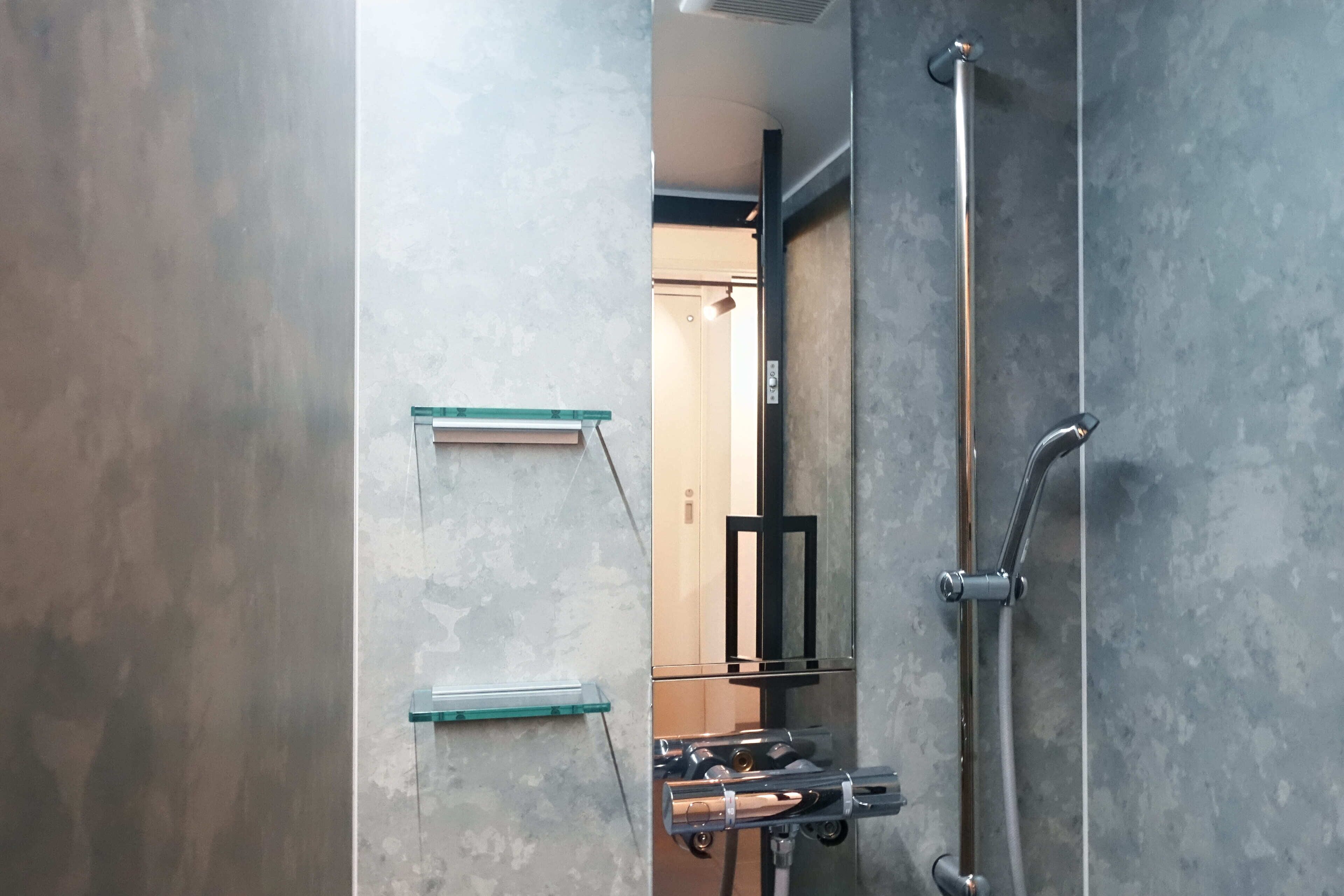 A modern bathroom with a glass shower enclosure, a handheld showerhead, and a glass shelf unit.