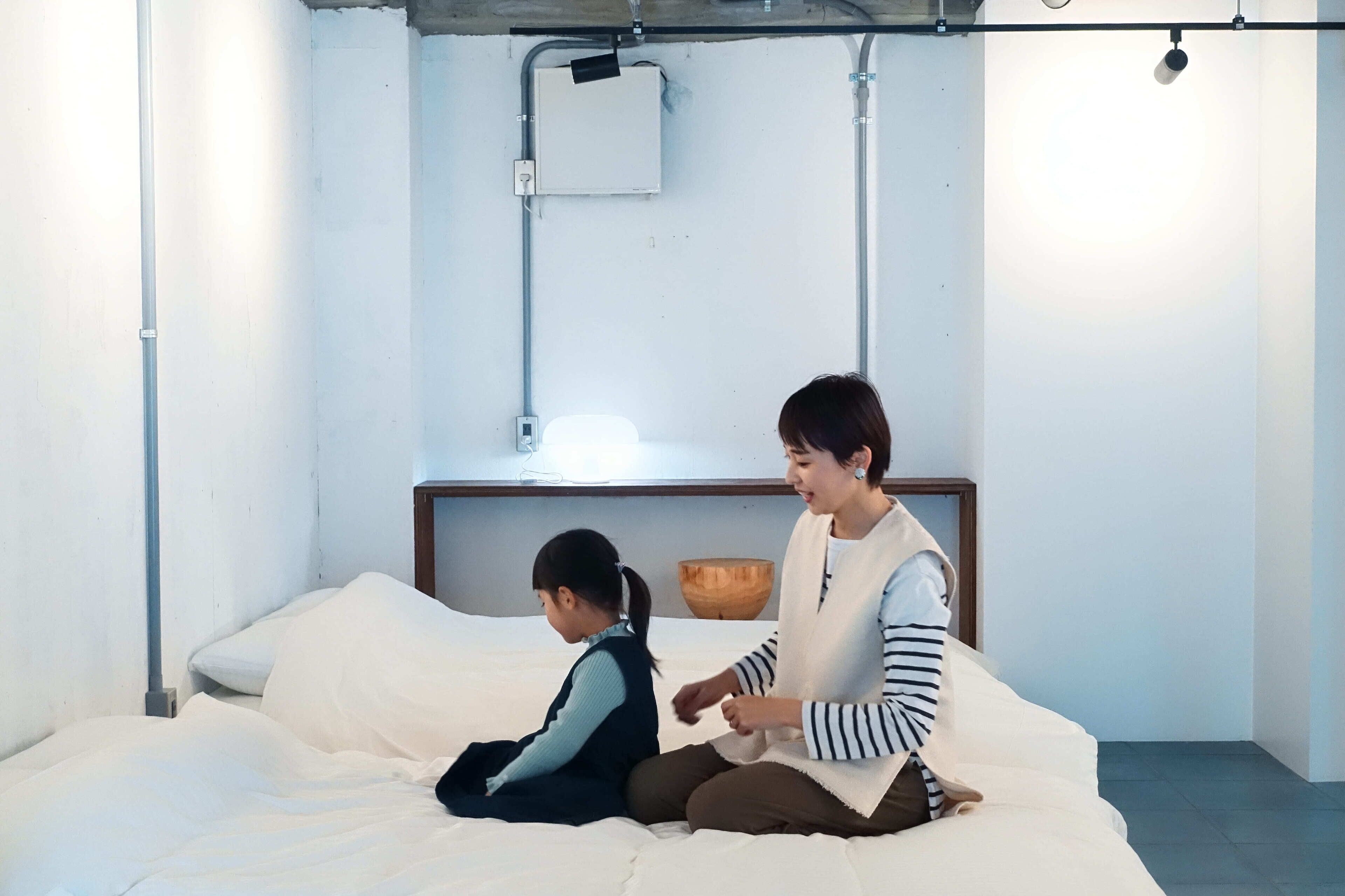 A room with a bed, a wooden bowl on a nightstand, and a wall-mounted light fixture.