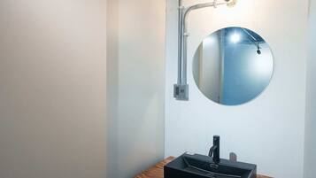 Une salle de bain avec un miroir rond, un meuble-lavabo en bois et un robinet fixé au mur.