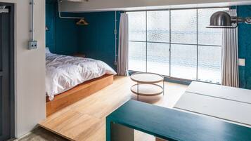 A compact bedroom with a bed, a small round table, and a window with a view of the water.