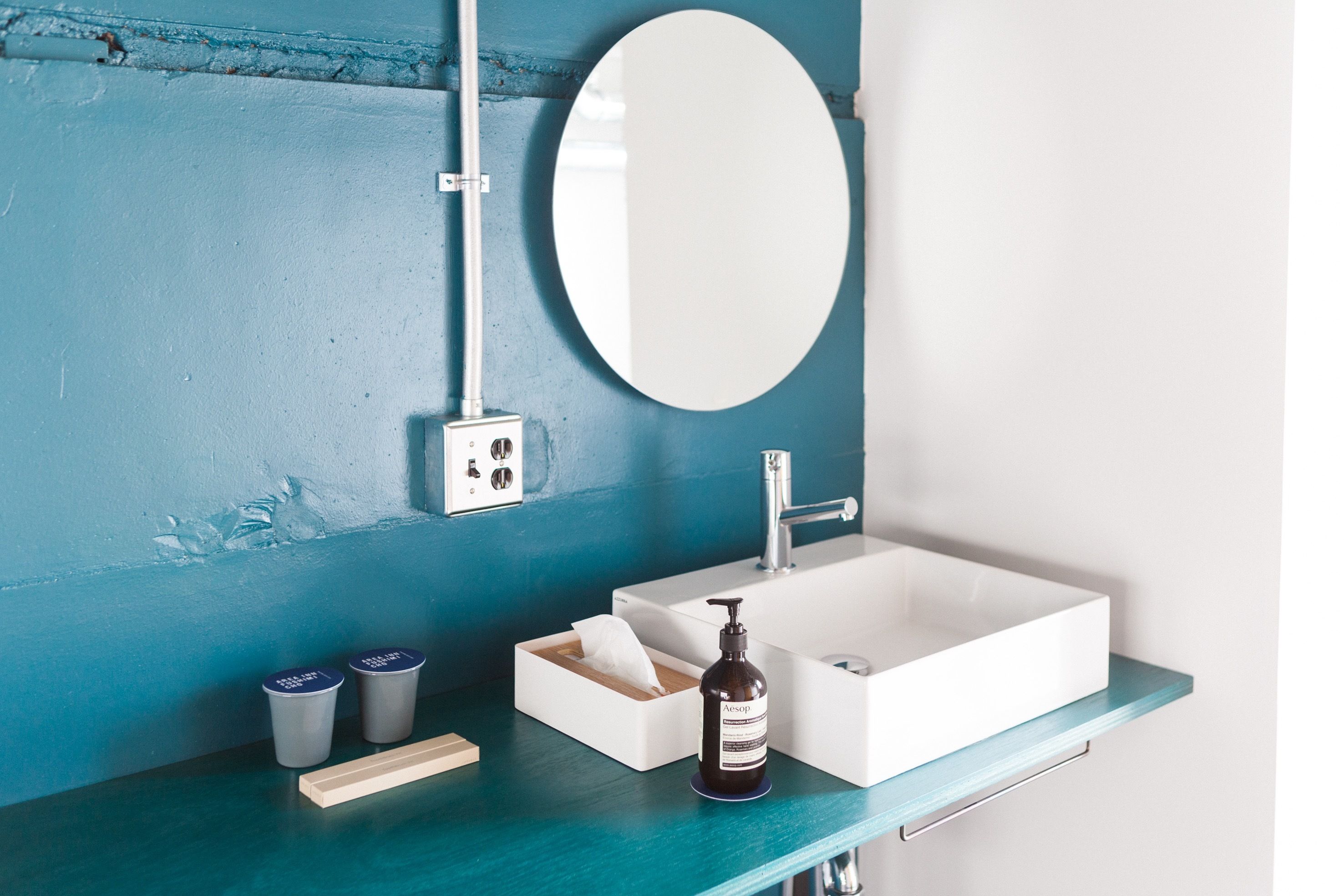 Un baño con lavamanos blanco, un espejo y encimera color turquesa. Hay dos recipientes sobre la encimera.