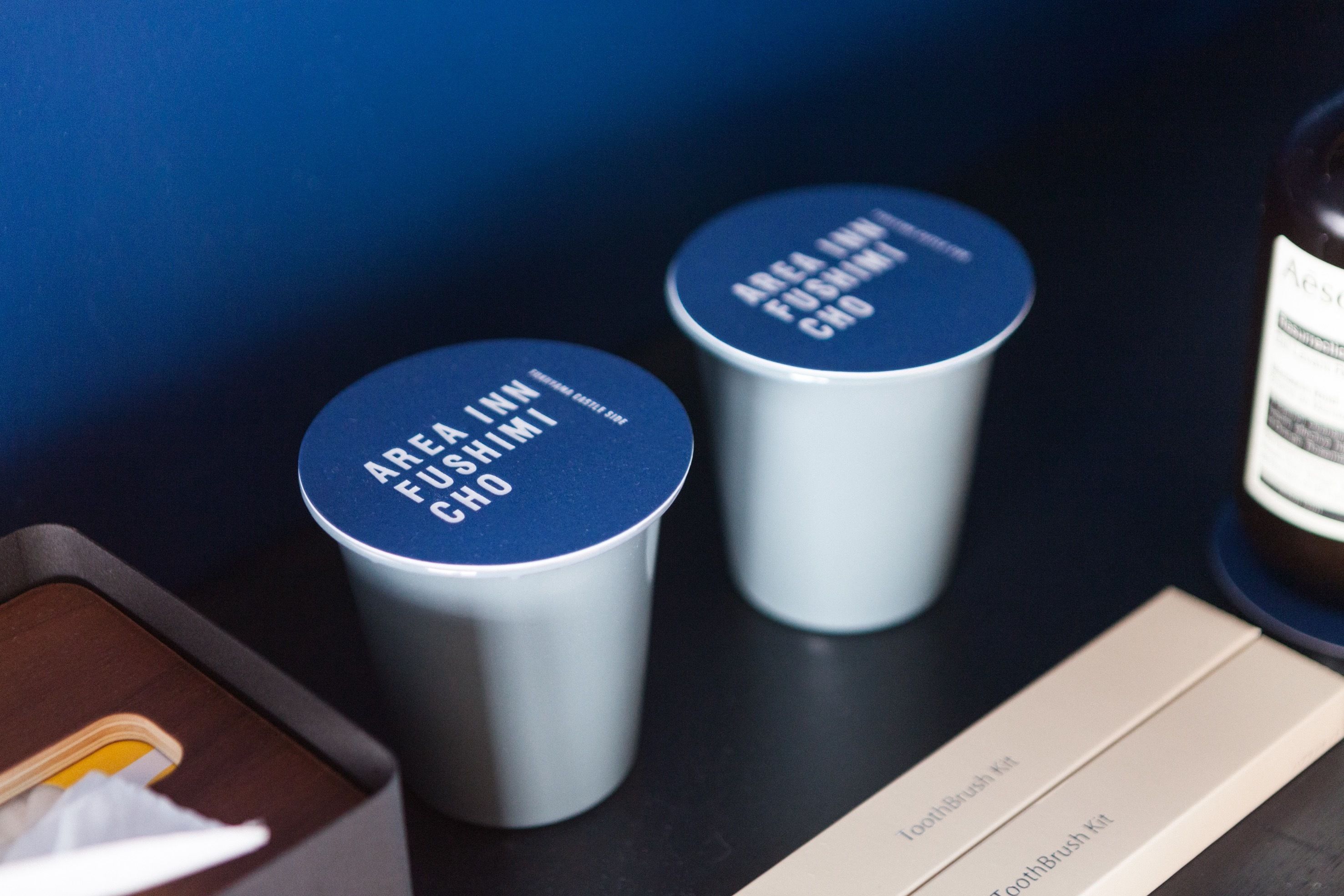 Two containers labeled "AREA INN FUSHIMI CHO" on a table with a tray and a bottle.