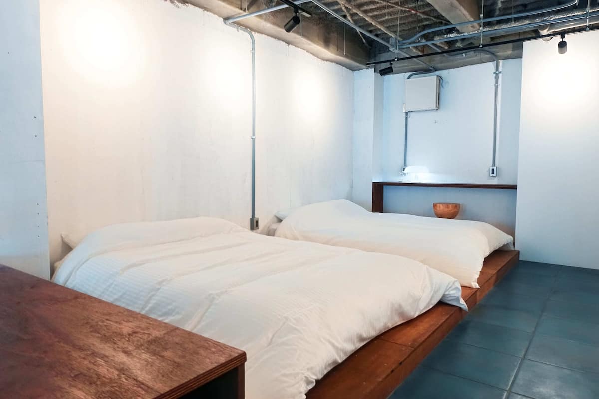 A room with two beds, a wooden table, and a small wooden shelf with a bowl.