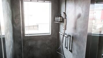 Un baño con un ventanal grande, una ducha con cabezal de ducha manual y un estante con artículos de aseo.