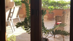 Une pièce dotée d’une porte-fenêtre coulissante donnant sur un patio extérieur agrémenté de plantes en pot et offrant une vue sur un plan d’eau et des collines.