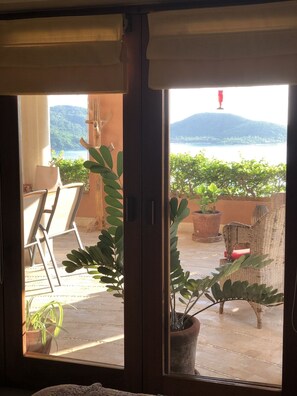 A room with a sliding glass door leading to an outdoor patio with potted plants and a view of a body of water and hills.