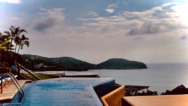 Une piscine avec vue sur la mer et les collines en arrière-plan.